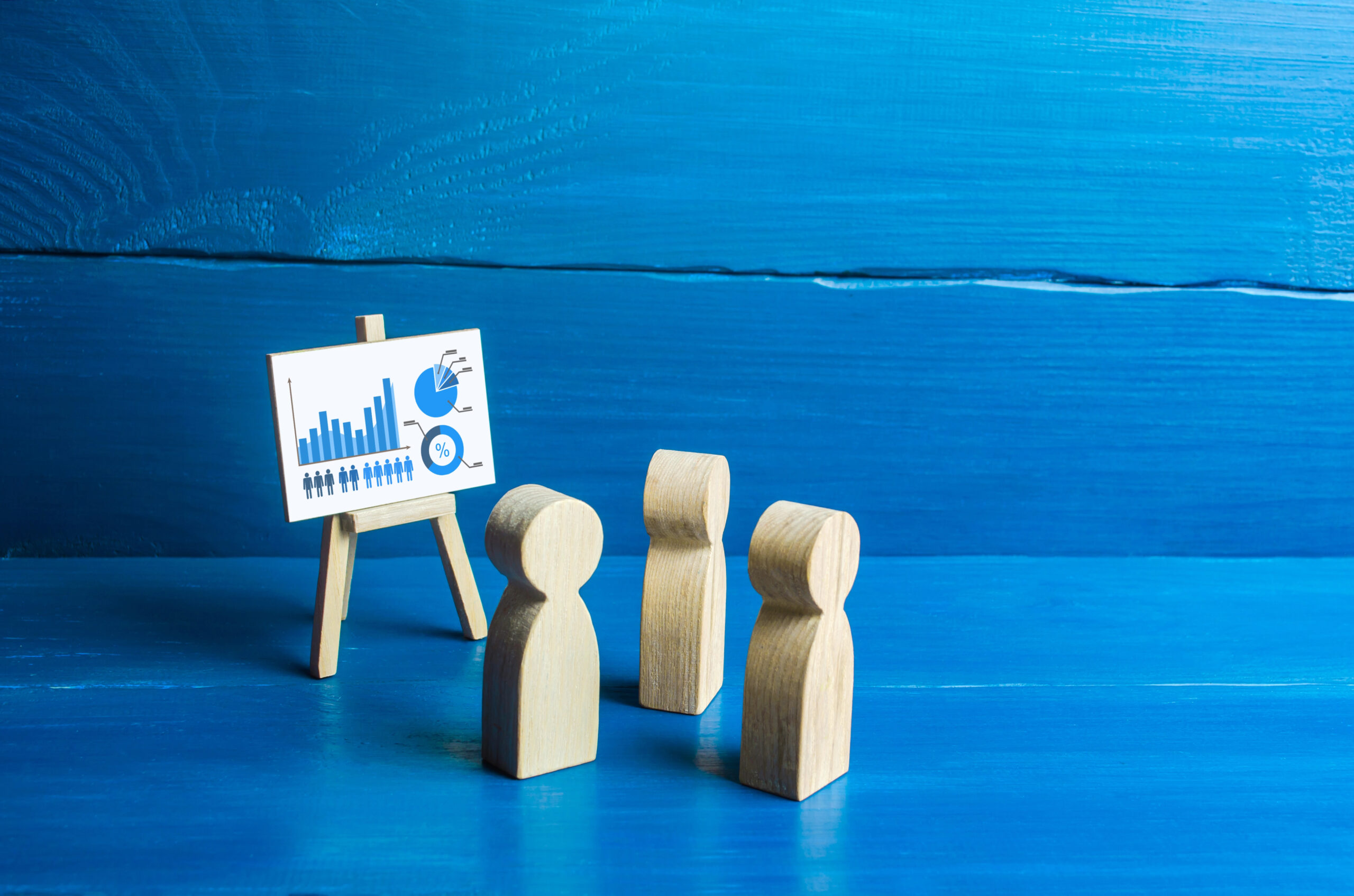 Wooden people near an easel with data graphs symbolizing what a data analyst is.