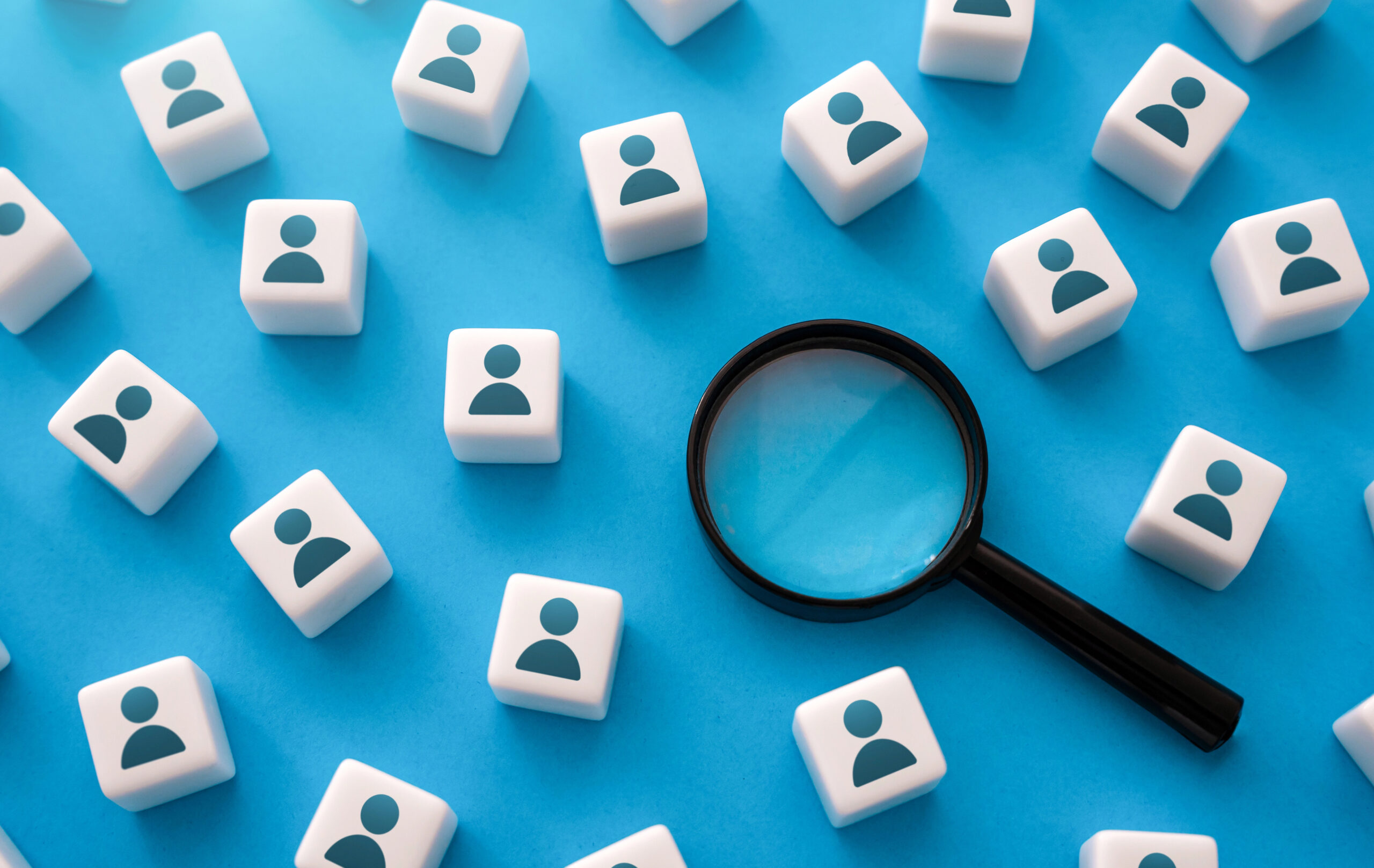 A magnifying glass in the middle of tiles with people on them symbolizing HMIS staffing struggles.